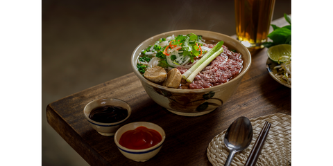 An inviting bowl of Pho soup, brimming with tender beef slices, fresh herbs, and rice noodles, all submerged in a rich, aromatic broth. For Noshejan's blog post titled A Journey of Flavor and Friendship.