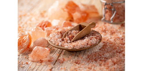 Pink Himalayan salt scattered in a styled manner, showcasing its coarse texture and beautiful pink hue against a contrasting background. For Noshejan's blog post titled Pretty In Pink.